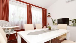 A modern dining area with a white table and chairs, red curtains, a clock, and a TV on the wall. - Zalazak Sunca by Interhome (Novigrad (Zadar))