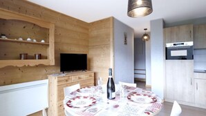 Una cucina moderna con mobili in legno, una TV integrata e un'area pranzo con un tavolo rotondo apparecchiato per due persone.