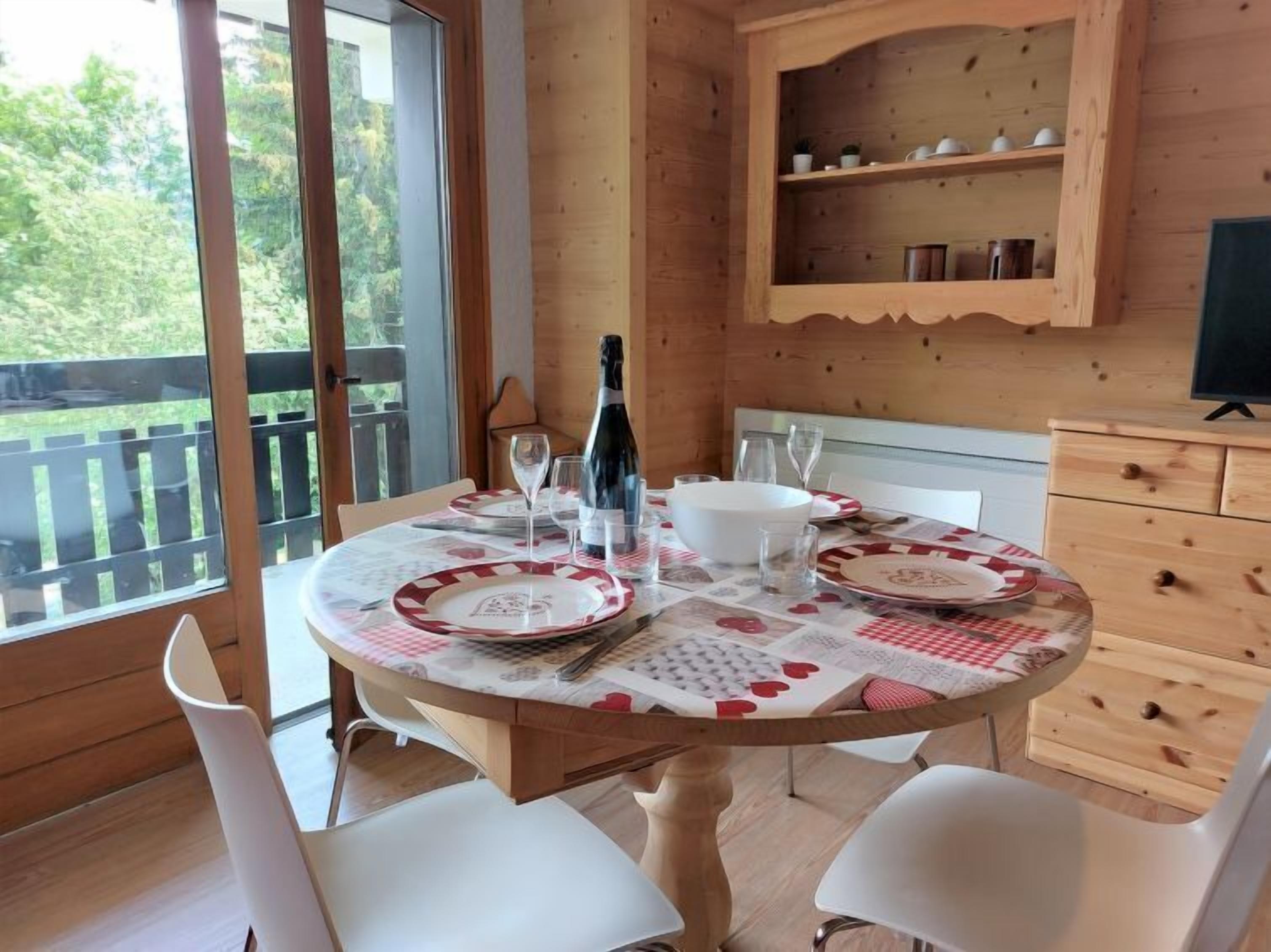 A dining area with a round table set for two, a bottle of champagne, and a wooden cabinet above the table.