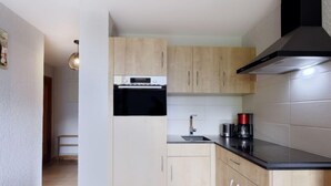 Una cucina compatta con mobili in legno, un piano di lavoro nero, una cappa aspirante in acciaio inossidabile e un forno integrato.