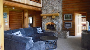A log cabin interior with a stone fireplace, wooden furniture, and a balcony.
