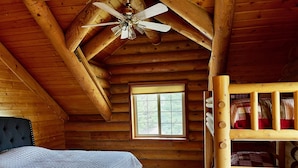 A log cabin bedroom with a bed, a bunk bed, a window, and a ceiling fan.