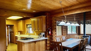 A log cabin interior with a kitchen and dining area, wooden walls, and a fireplace.