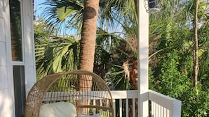 A porch with a wicker swing chair, a small round table, and a potted plant. - Delightful Cottage in Historic Downtown St. Augustine Florida (St. Augustine)