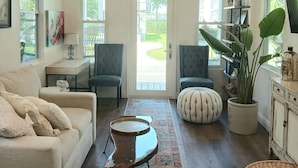 A spacious living room with a ceiling fan, a sofa, a coffee table, and a large window. - Delightful Cottage in Historic Downtown St. Augustine Florida (St. Augustine)