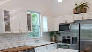 A modern kitchen with white cabinets, a marble countertop, and a stainless steel refrigerator. - Delightful Cottage in Historic Downtown St. Augustine Florida (St. Augustine)