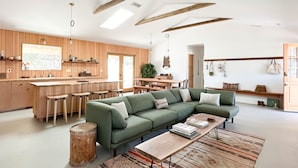A modern living room with a green sectional sofa, wooden bar, and a large window.