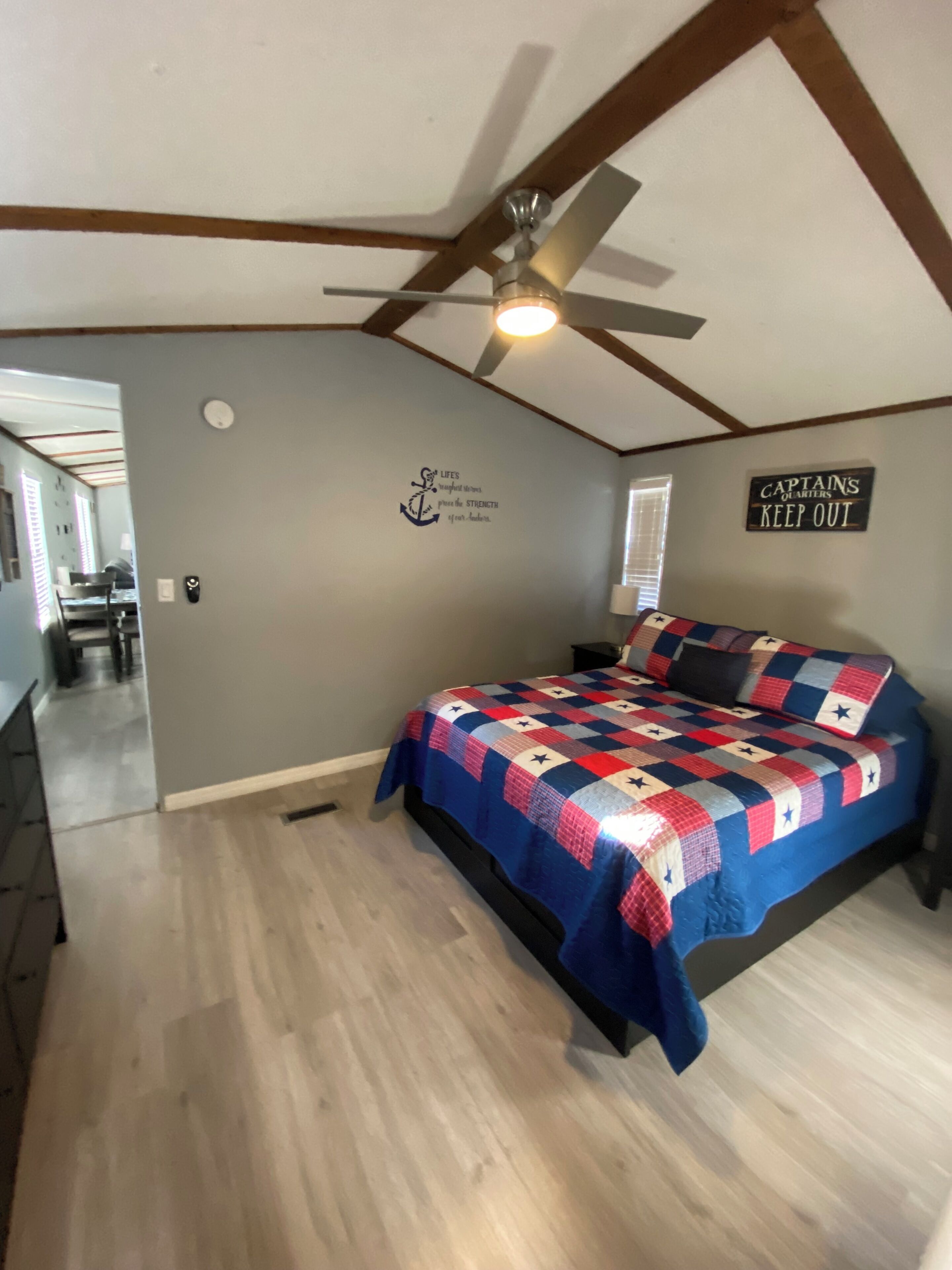 A bedroom with a bed, a ceiling fan, a wall with a nautical-themed decal, and a sign that says "CAPTANS QUARTERS KEEP OUT".