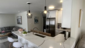 Une cuisine moderne dotée d’un îlot central, de tabourets de bar, d’appareils électroménagers en acier inoxydable et de luminaires suspendus.