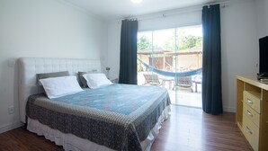 A bedroom with a bed, a desk, and a view of an outdoor hammock and patio. - Clim House in Buzios  (Altos de Búzios Armação dos Búzios)
