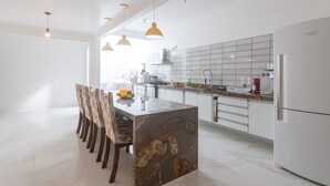 A modern kitchen with a marble island, pendant lights, and a white refrigerator. - Clim House in Buzios  (Altos de Búzios Armação dos Búzios)