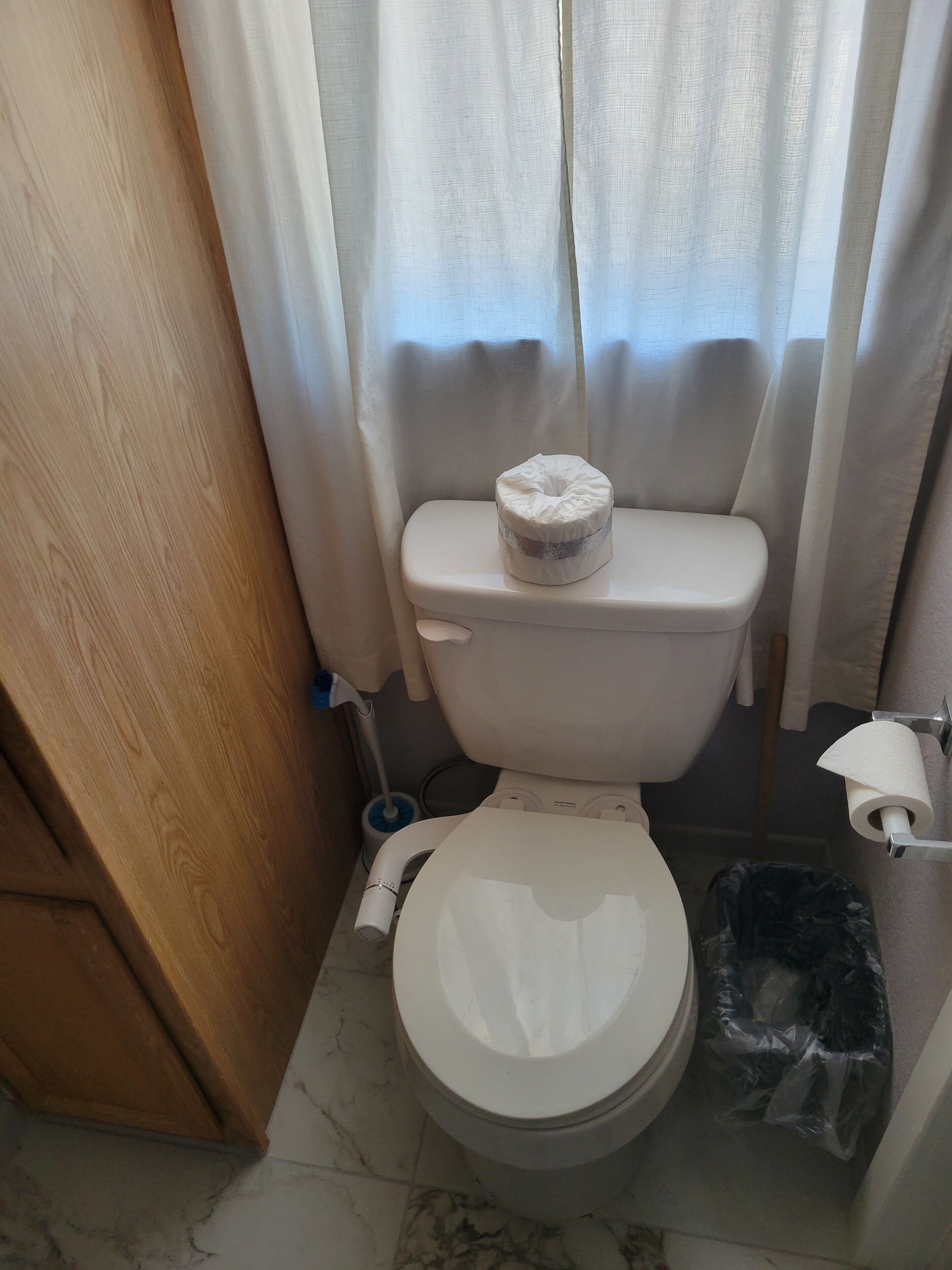 A bathroom with a toilet, a bidet, a toilet paper holder, and a trash bin.
