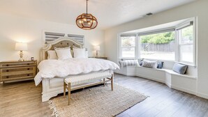 Une chambre à coucher avec un grand lit, des tables de chevet, un banc, un coin fenêtre aménagé en siège et un luminaire suspendu.