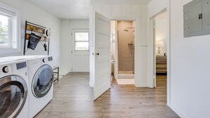 Un espace buanderie comprenant un lave-linge, un étendoir et un étendoir mural avec un chapeau et un sac à linge.
