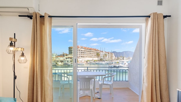 A balcony with a table and chairs, a view of a marina, and a building with balconies in the background.