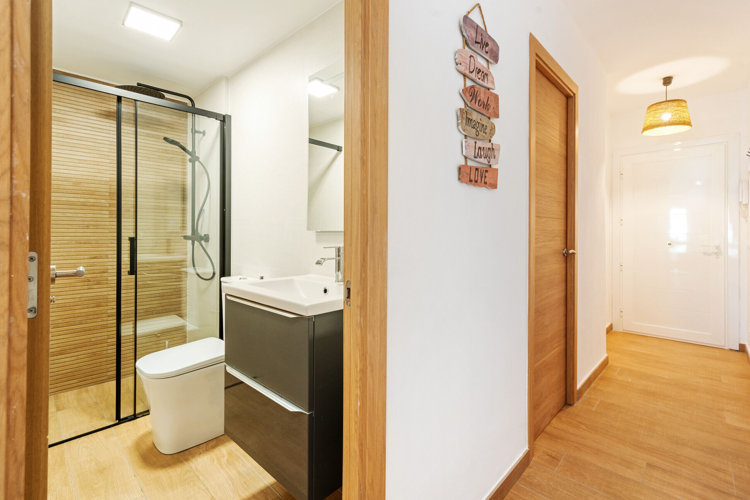 A modern bathroom with a glass shower enclosure, a white toilet, and a stainless steel sink.