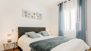 A bedroom with a bed, a bedside table, a wall-mounted artwork, and a window with curtains.