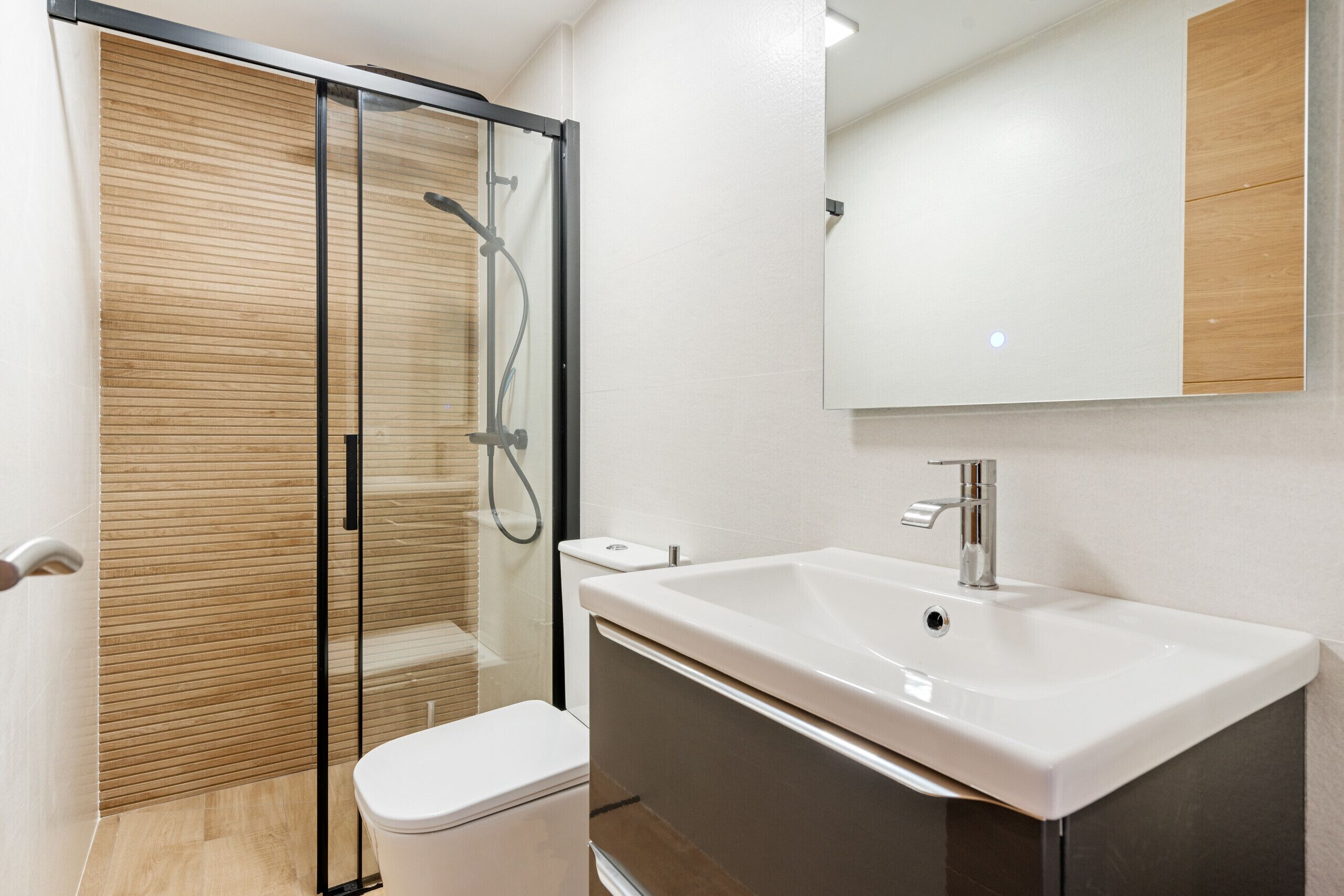 Ein modernes Badezimmer mit Duschkabine aus Glas, einem weißen Waschbecken und einer Toilette.