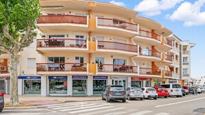 Um edifício com vários andares, varandas, lojas e carros estacionados.