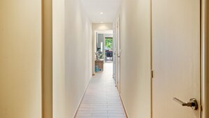 Um corredor estreito com piso de madeira que leva a um quarto com porta.