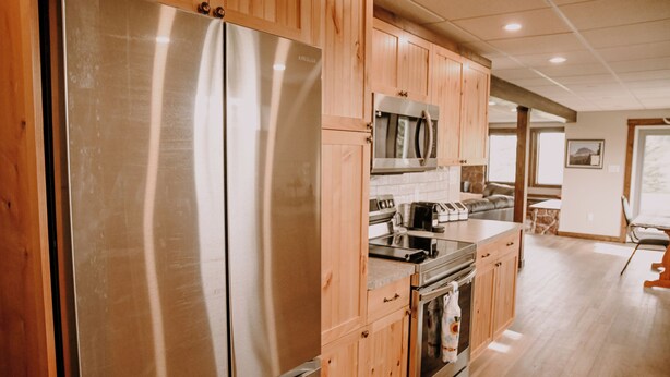 A modern kitchen with wooden cabinets, stainless steel appliances, and a large refrigerator. - Old Chief Bunkhouse - ranch with views of Chief Mountain (Cardston)