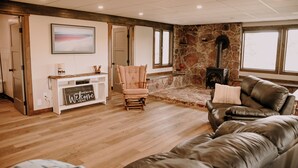 A spacious living room with a stone fireplace, a wooden console table with a 'Welcome' sign, a leather sofa, and a cushioned armchair. - Old Chief Bunkhouse - ranch with views of Chief Mountain (Cardston)