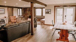 A spacious living area with a large sectional sofa, a dining table with chairs, and a stone fireplace. - Old Chief Bunkhouse - ranch with views of Chief Mountain (Cardston)