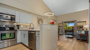 A modern kitchen with stainless steel appliances, white cabinetry, and a central island with a vase of flowers. - Modern & Tropical Oceanside Vistas  (Kihei)
