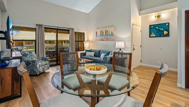 A modern living room with a glass dining table, a sofa, and a TV. - Modern & Tropical Oceanside Vistas  (Kihei)