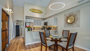 A modern kitchen with a central island, wooden chairs, and a decorative wall piece. - Modern & Tropical Oceanside Vistas  (Kihei)