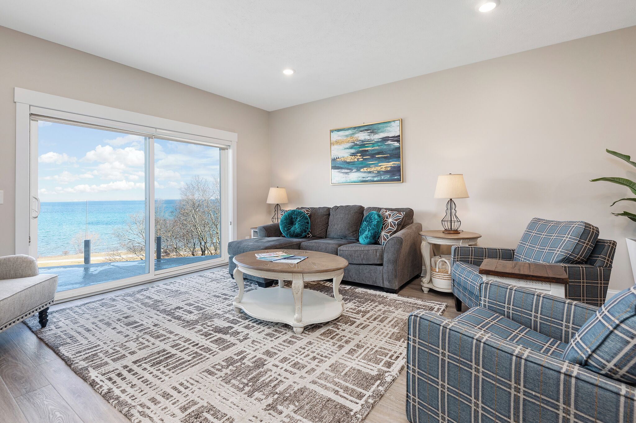 Sala de estar con sofá, sillón, mesa de centro y vista al mar a través de amplios ventanales.