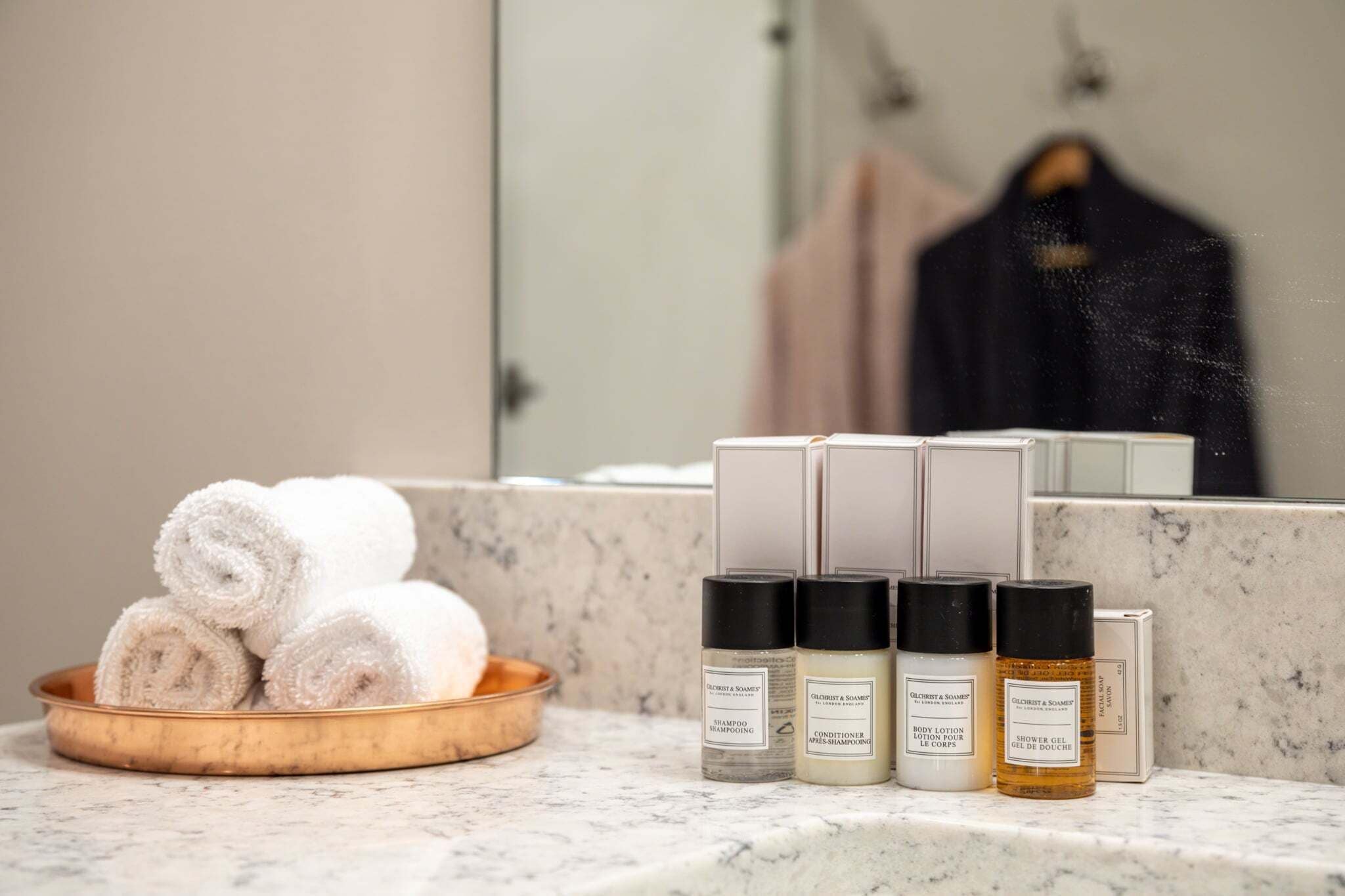 A bathroom with a marble countertop, a bowl of rolled towels, and three bottles of toiletries.
