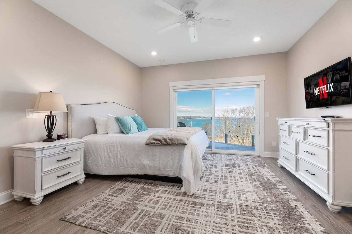 A bedroom with a bed, nightstand, dresser, TV, and a view of the outdoors.