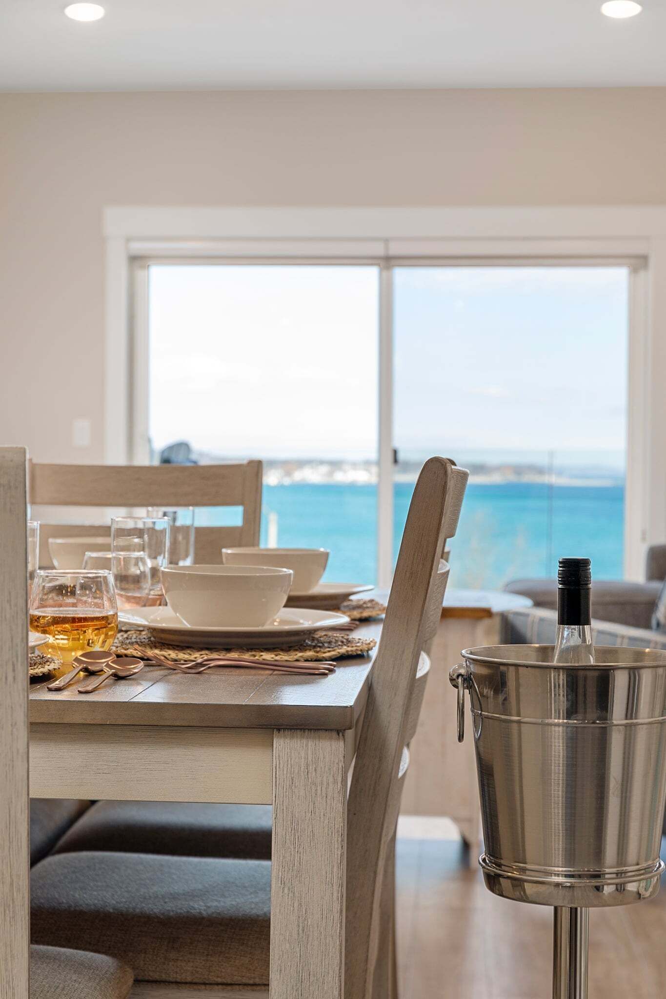 Una mesa de comedor con vista al océano, un cubo de metal y un vaso de bebida.