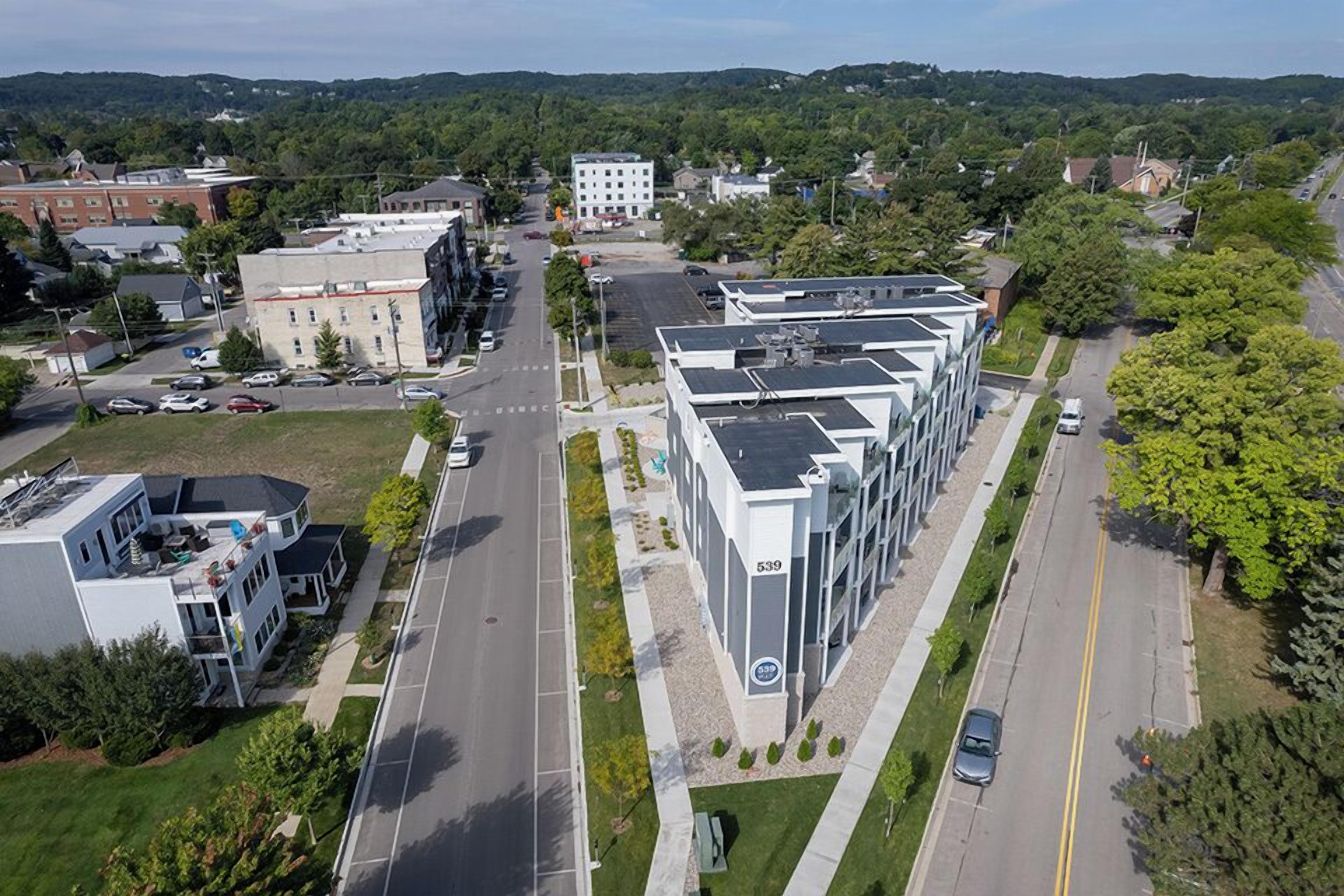 An aerial view of a modern building complex with multiple floors, a parking lot, and surrounding greenery.