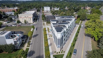 An aerial view of a modern building complex with multiple floors, a parking lot, and surrounding greenery.
