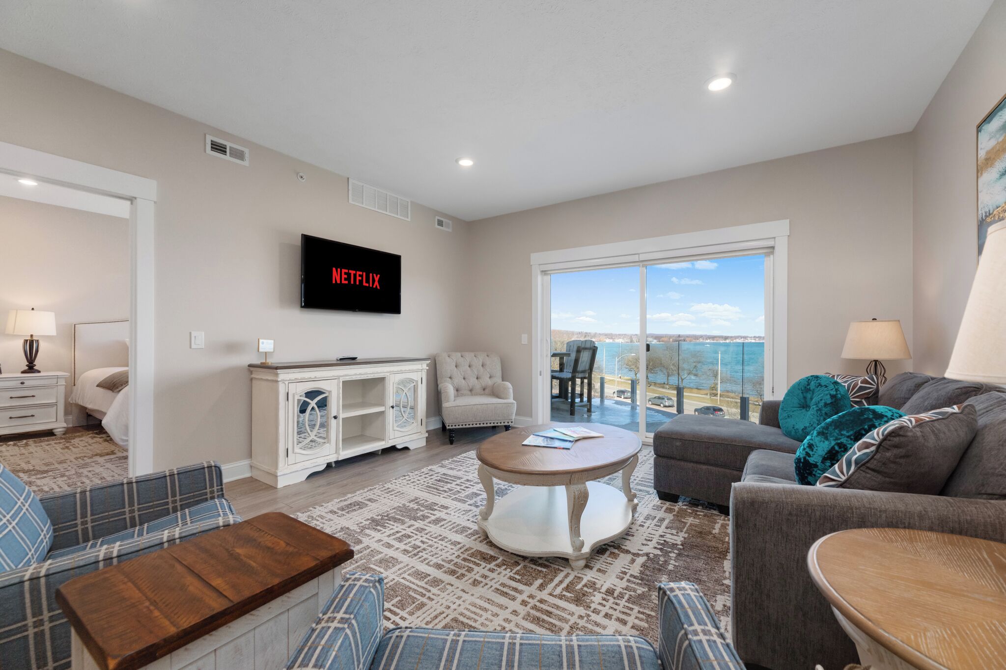 A living room with a flat-screen TV, a sofa, a coffee table, and a view of the outdoors.