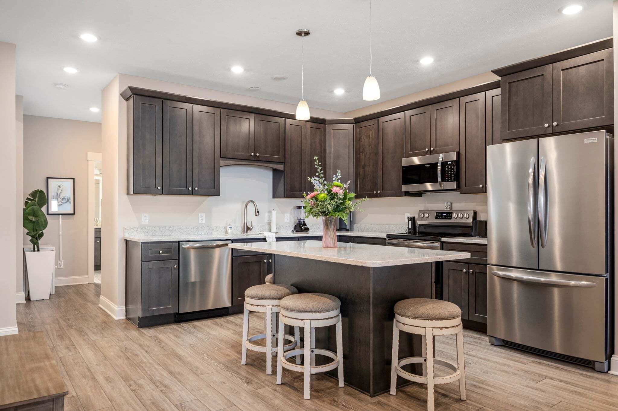 A modern kitchen with dark cabinets, stainless steel appliances, and a central island with stools.