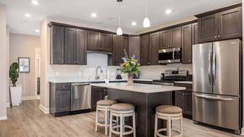 A modern kitchen with dark cabinets, stainless steel appliances, and a central island with stools.