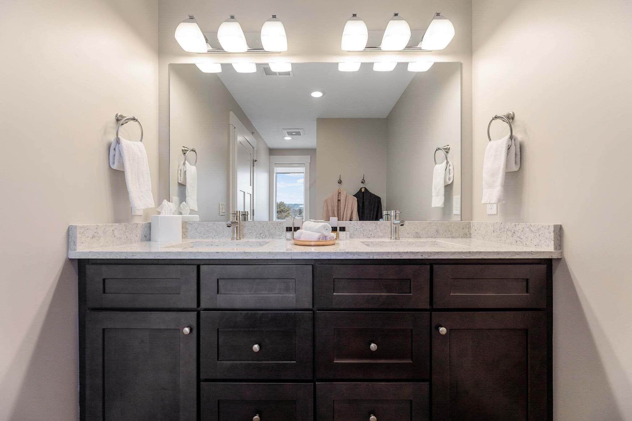 A bathroom with a large mirror, two sinks, dark cabinets, and a towel rack.