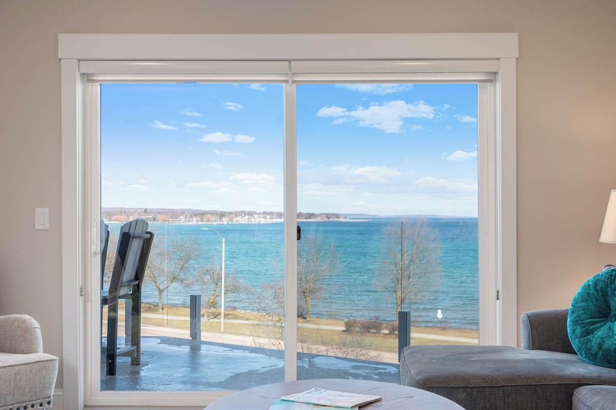 A room with a large sliding glass door leading to a view of a body of water and a distant shoreline.