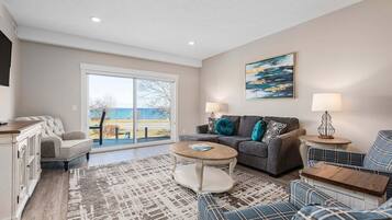A living room with a sofa, a coffee table, a TV, and a view through a large window.