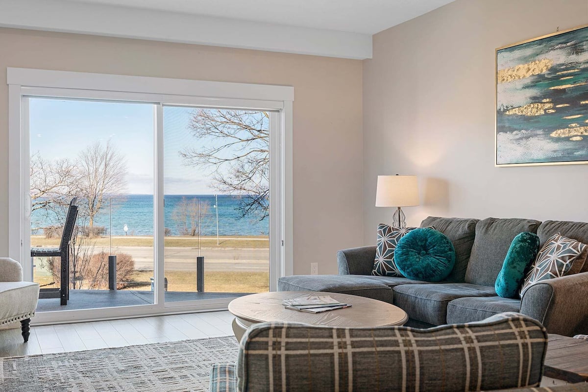 A living room with a sofa, a round coffee table, and a bench. There is a large window with a view of the outdoors.