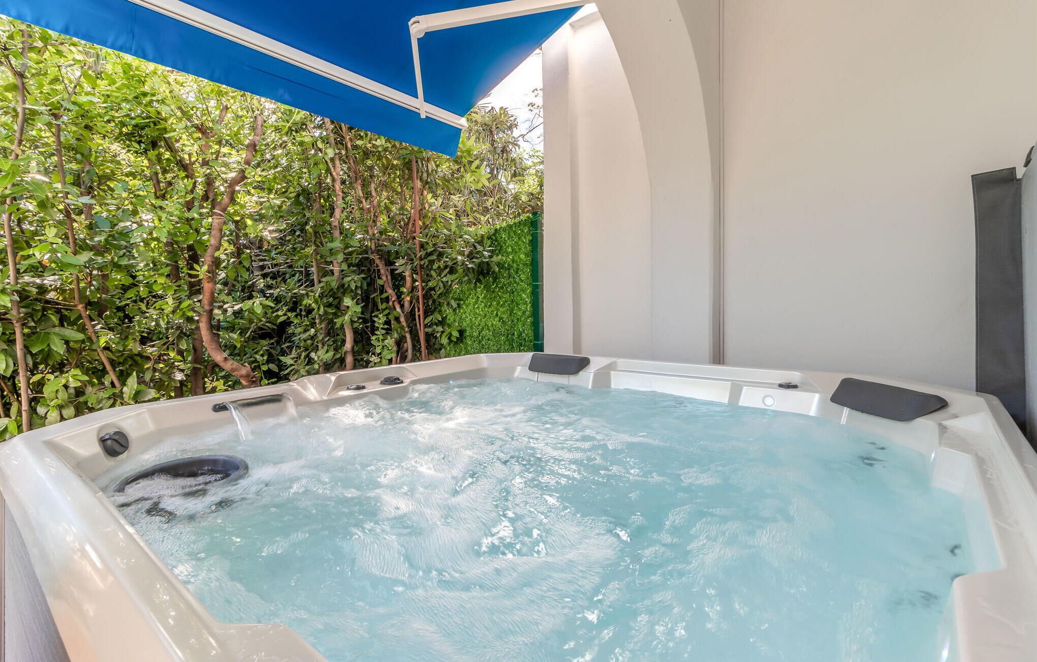 A hot tub with a view of a lush green hedge and a white wall.