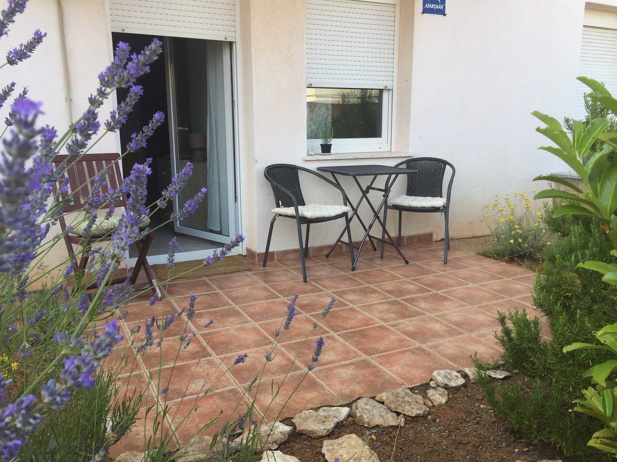 An outdoor patio with a table and chairs, surrounded by a garden with lavender plants and a small rock garden.