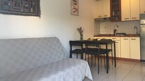 Un salon avec un canapé, une table à manger avec des chaises et un coin cuisine équipé de placards et d’un réfrigérateur.