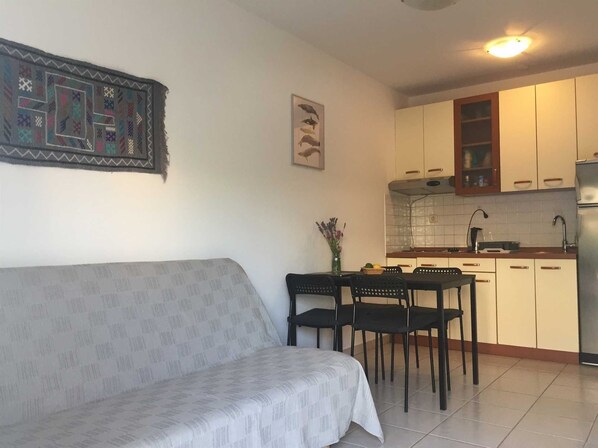 Una sala de estar con sofá, una mesa de comedor con sillas y una zona de cocina con armarios y un refrigerador.