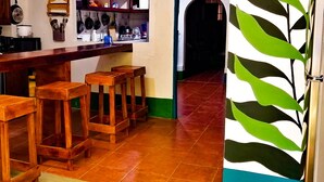A kitchen with a wooden bar and stools, a gas stove, and a variety of kitchen utensils on the wall. - Hostal El Rio (León)
