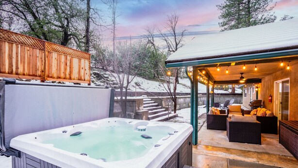 Ein Whirlpool und eine Sitzgelegenheit im Freien mit einer überdachten Terrasse, umgeben von Schnee und Bäumen.
