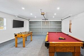 Une pièce équipée d’une table de billard, d’un baby-foot et d’un téléviseur fixé au mur.